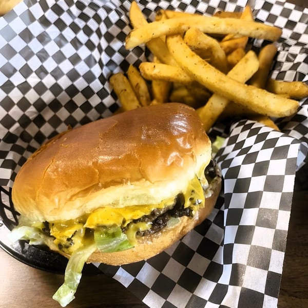 A cheeseburger with lettuce and fries served in a black and white checkered basket.