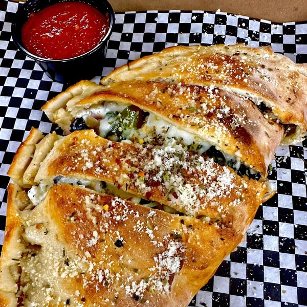 Sliced calzone with melted cheese, herbs, and a side of marinara sauce on checkered paper.