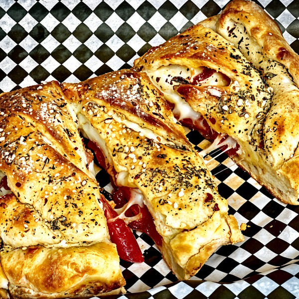 Sliced pepperoni and cheese stromboli with herbs and parmesan, served on checkered paper.